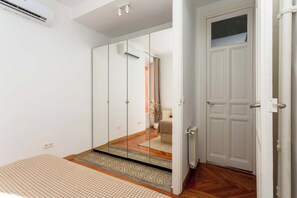 A bedroom with a bed, a wardrobe, a mirror, and a door. - A two-bedroom, chef's kitchen home in one of Madrid's most elegant quarters, where an open-plan living space built for hosting sits steps from the city's trendiest shops and restaurants. (MADRID)