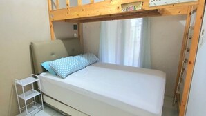 Un lit superposé avec une tête de lit, une petite étagère blanche et une fenêtre avec des rideaux.