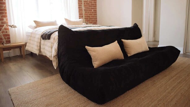 A bedroom with a black sofa, a bed with a striped blanket, and a brick wall. - The Brick Studio in Los Feliz (Los Angeles)