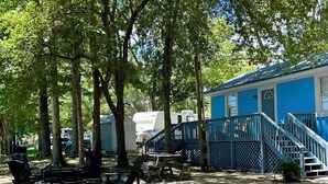 Een camping met een blauw gebouw, een houten terras en campers.