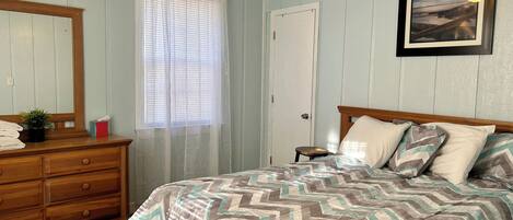 A bedroom with a bed, wooden dresser, and a ceiling fan.