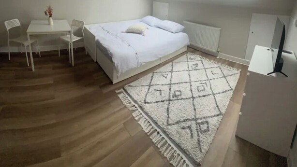 Une chambre à coucher comprenant un lit, un bureau, deux chaises, un radiateur, une lampe et une lucarne.