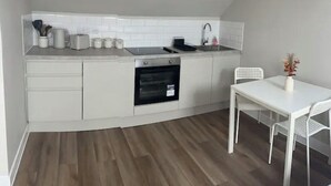 Une cuisine compacte avec des meubles blancs, un four encastré et une table à manger blanche avec des chaises.