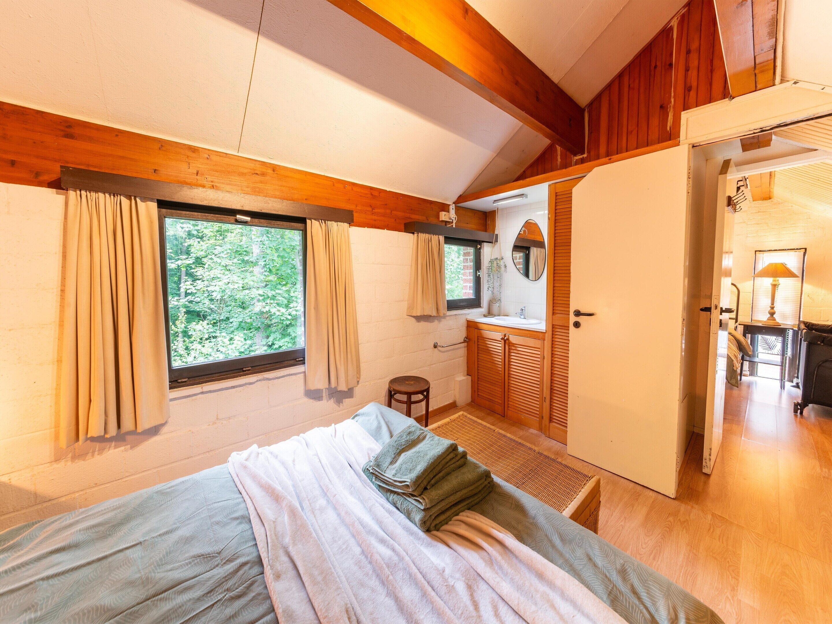 Ein Schlafzimmer mit Bett, einem Vorhangfenster, einer Holzbalkendecke und Blick auf Grünfläche.