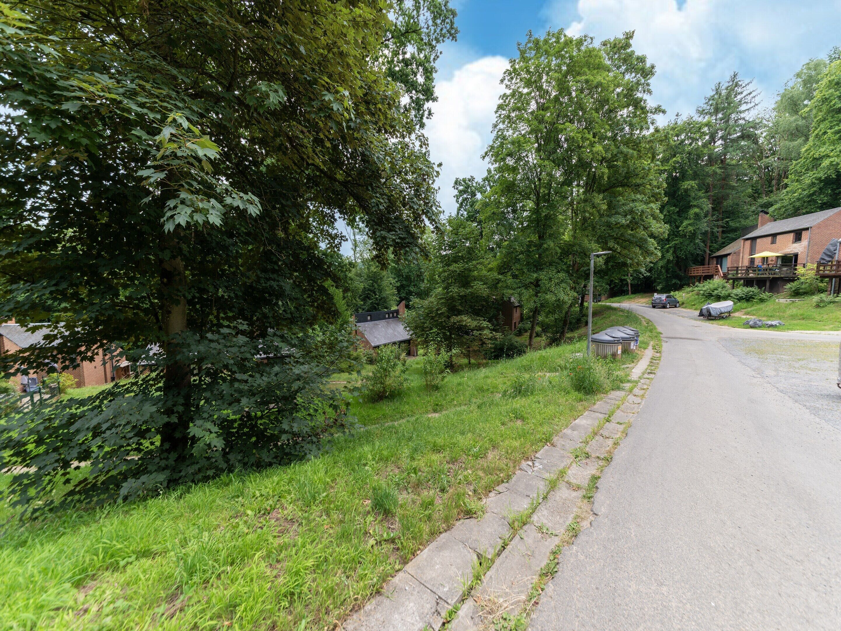 Eine Landstraße mit einer grünen Böschung, Bäumen und einem Gebäude mit Veranda.