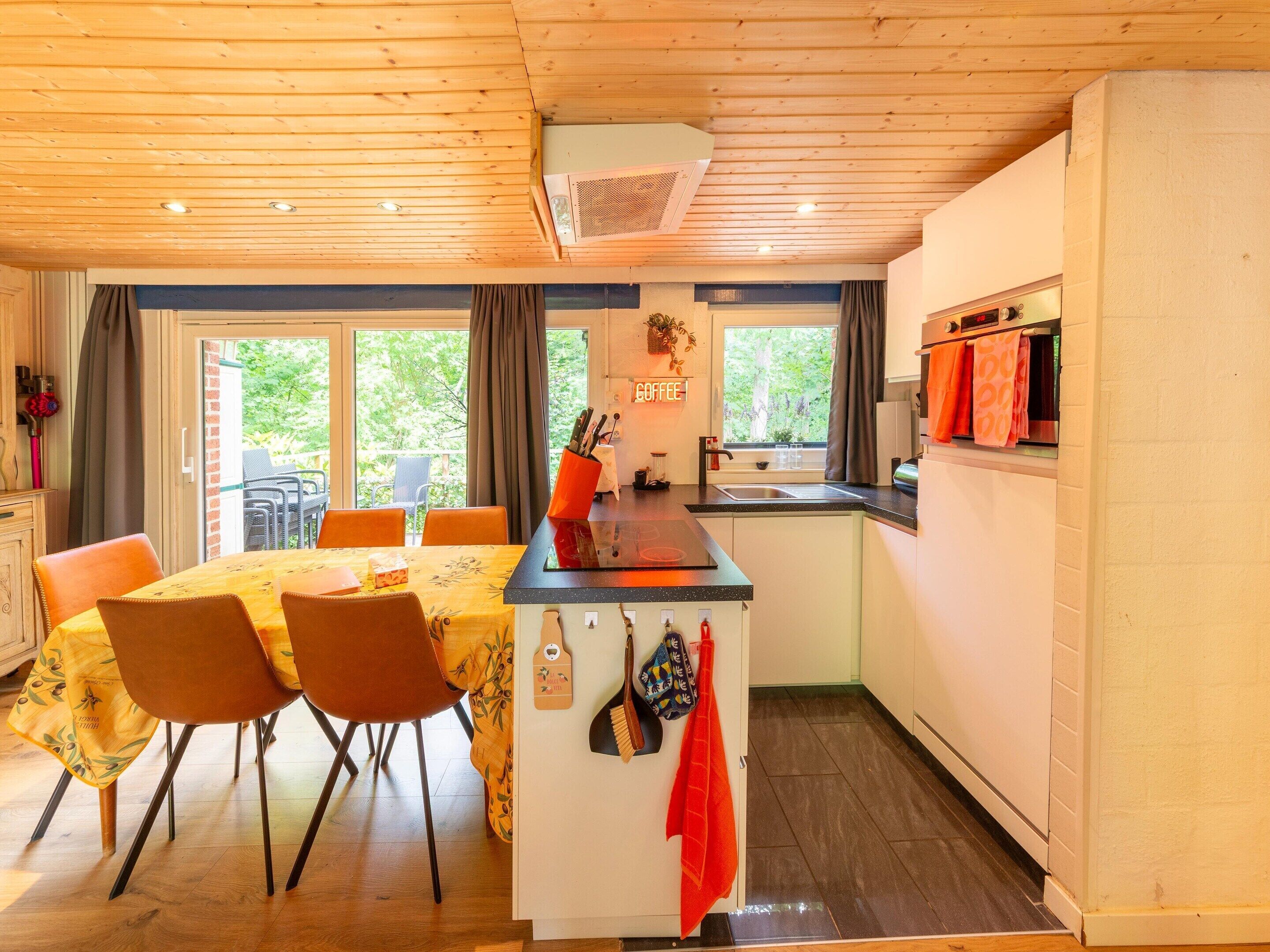 A cozy kitchen with a dining area, wooden ceiling, and large windows.
