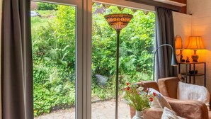 A room with a large sliding glass door leading to a garden, a table lamp, and a sofa with cushions. - Chalet in Hastiere Near Castle (Hastiere)