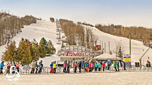 A ski resort with a chairlift, a sign reading "RILLION," and a crowd of people at the bottom of the slope. - Blue Mountain Suites (Blue Mountain)