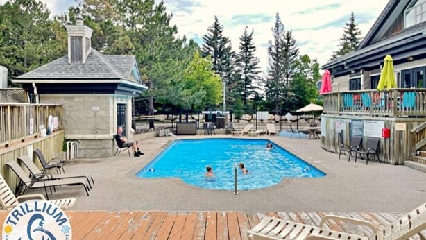 A swimming pool with lounge chairs and umbrellas, surrounded by wooden deck and trees. - Blue Mountain Suites (Blue Mountain)