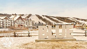 A resort with multiple buildings, a ski slope, and a large 'BLUE' sign in the foreground. - Blue Mountain Suites (Blue Mountain)