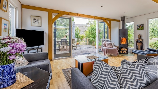Een ruime woonkamer met een open haard, een televisie en een groot raam met uitzicht op een tuin.
