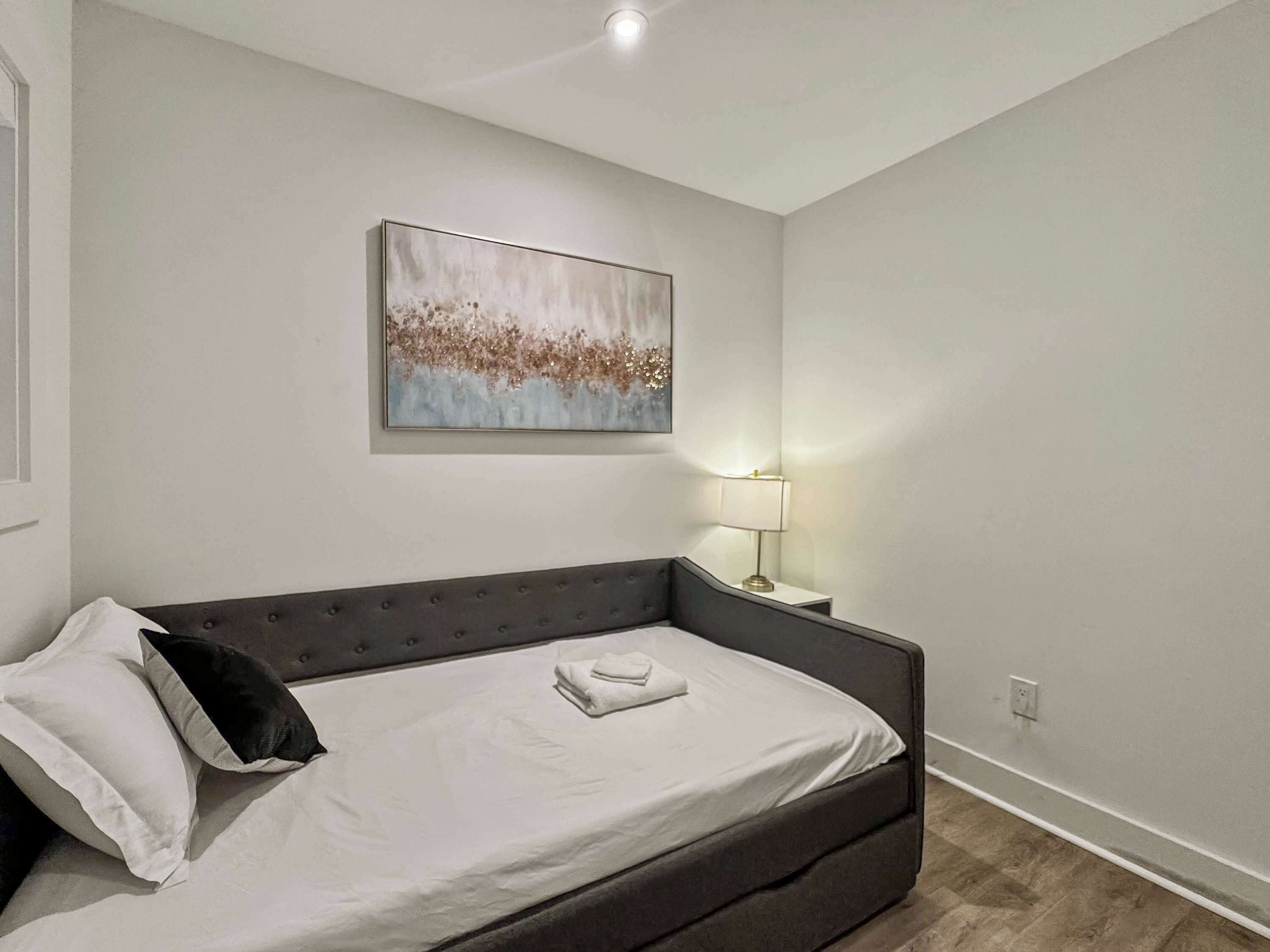 Ein modernes Schlafzimmer mit einem dunkelbraunen Schlafsofa, einem weißen Kissen, einem gefalteten weißen Handtuch und einer Wandlampe.