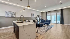 A modern apartment with a kitchen island, a living area with a sofa and a coffee table, and large windows offering a view.