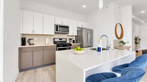 A modern kitchen with white cabinets, a stainless steel refrigerator, a microwave, and a stove.