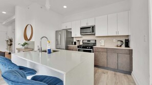 A modern kitchen with white cabinets, a stainless steel refrigerator, a microwave, a stove, and a coffee maker. - Stylish 3BD | Sleeps 6 | Northern Liberties (Philadelphia)