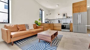 Un salon moderne avec un canapé en cuir, une table basse en bois et une cuisine équipée d’un réfrigérateur, d’un four et de placards.