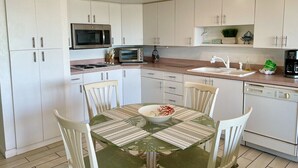 A modern kitchen with white cabinets, a microwave, an oven, a dishwasher, and a dining table with chairs.