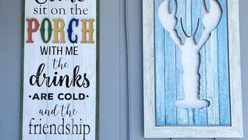 A wall with two decorative signs: one with a colorful text inviting someone to sit on the porch, and another with a white silhouette of a lobster.