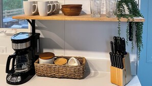 A kitchen with white cabinets, a coffee maker, a basket of coffee cups, and a knife block.