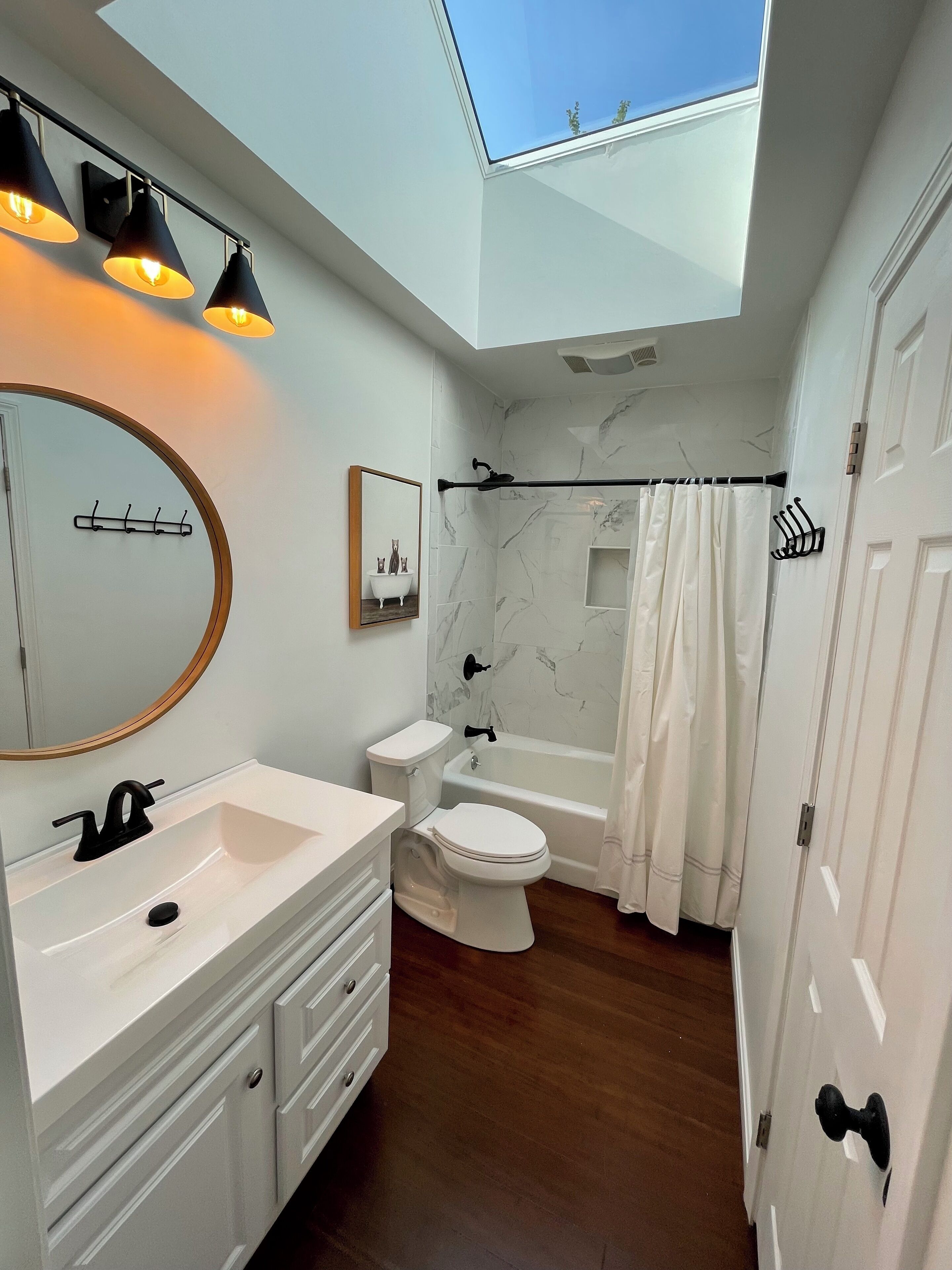 A modern bathroom with a skylight, a white vanity, a toilet, a bathtub, and a shower curtain.