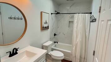 A modern bathroom with a skylight, a white vanity, a toilet, a bathtub, and a shower curtain.
