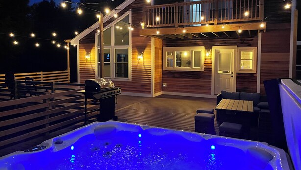 A wooden house with a hot tub, outdoor seating, and string lights.