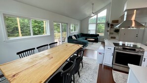 A modern kitchen with a wooden dining table, black chairs, a green sectional sofa, and a large window.