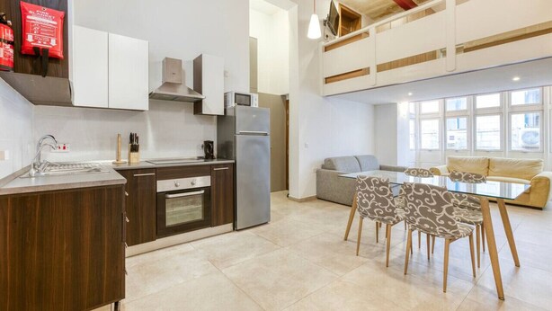 A modern kitchen with a dining area, featuring a built-in oven, a refrigerator, and a dining table with patterned chairs. - Charming, designer 1 bedroom Valletta Loft (Valletta)