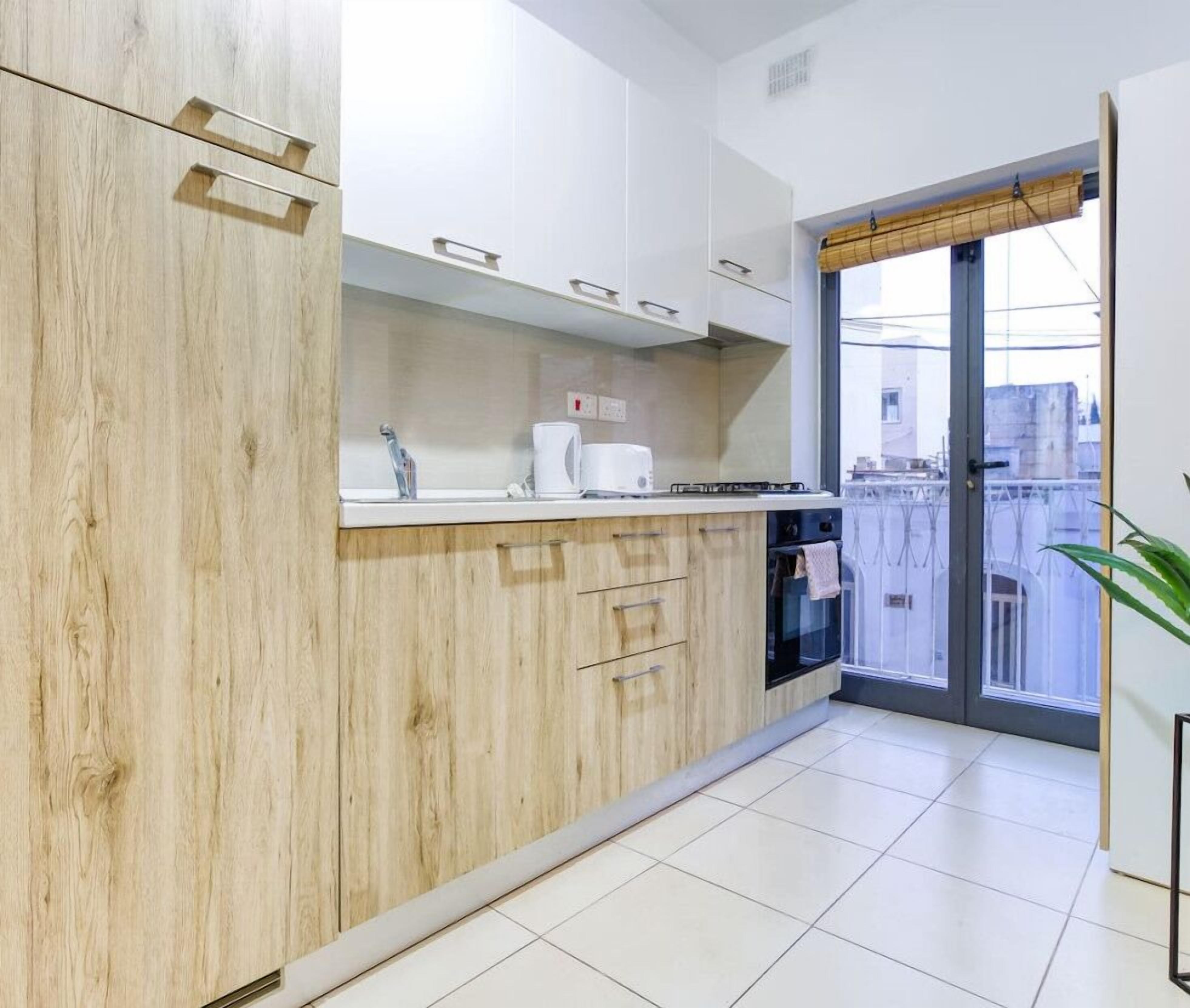 Une cuisine moderne avec des meubles en bois, un plan de travail blanc et une vue sur la ville grâce à une grande fenêtre.