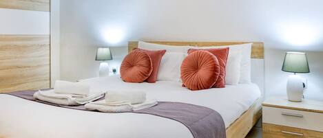 A neatly made bed with white linens and two pink decorative pillows, a wooden headboard, and two bedside lamps.