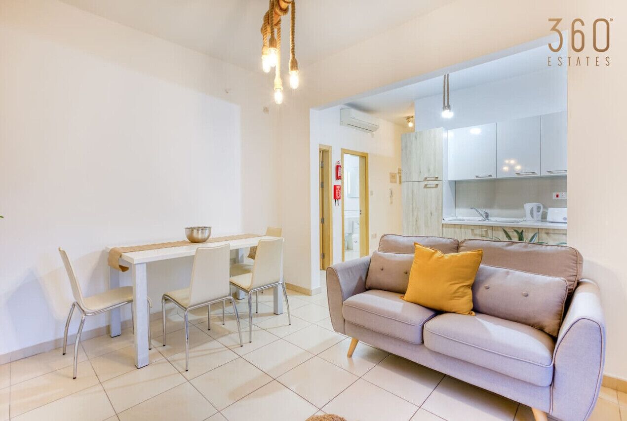 Un salon moderne avec un canapé, une table à manger et des chaises. On aperçoit un coin cuisine à l’arrière-plan.