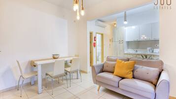 Un salon moderne avec un canapé, une table à manger et des chaises. On aperçoit un coin cuisine à l’arrière-plan.