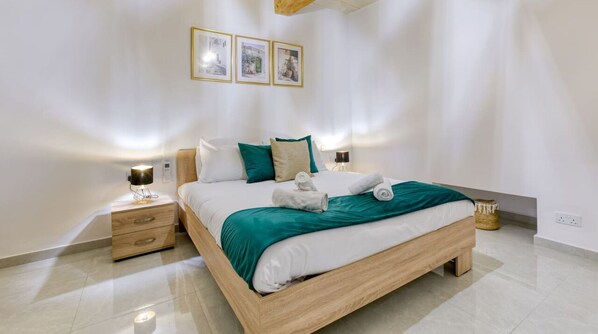 A modern bedroom with a wooden bed, white bedding, teal throw, and two bedside lamps.