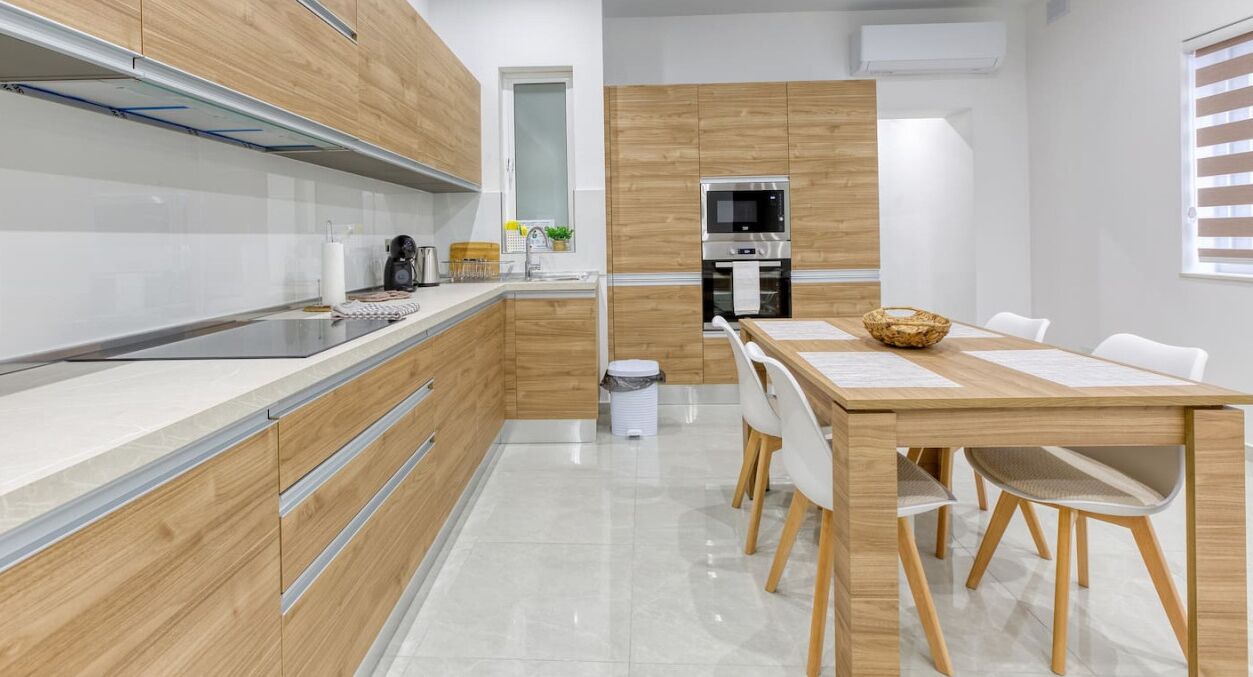A modern kitchen with wooden cabinets, a stainless steel sink, a microwave, and a dining table with chairs.