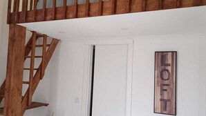 Un interior modern amb una escala de fusta, una taula rodona de fusta, un sofà gris amb un coixí colorit i un cartell penjat a la paret.