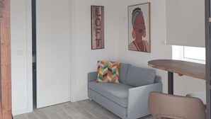 Un saló modern amb un sofà gris, un coixí estampat amb dibuixos geomètrics, una taula de fusta i una obra d'art emmarcada a la paret.