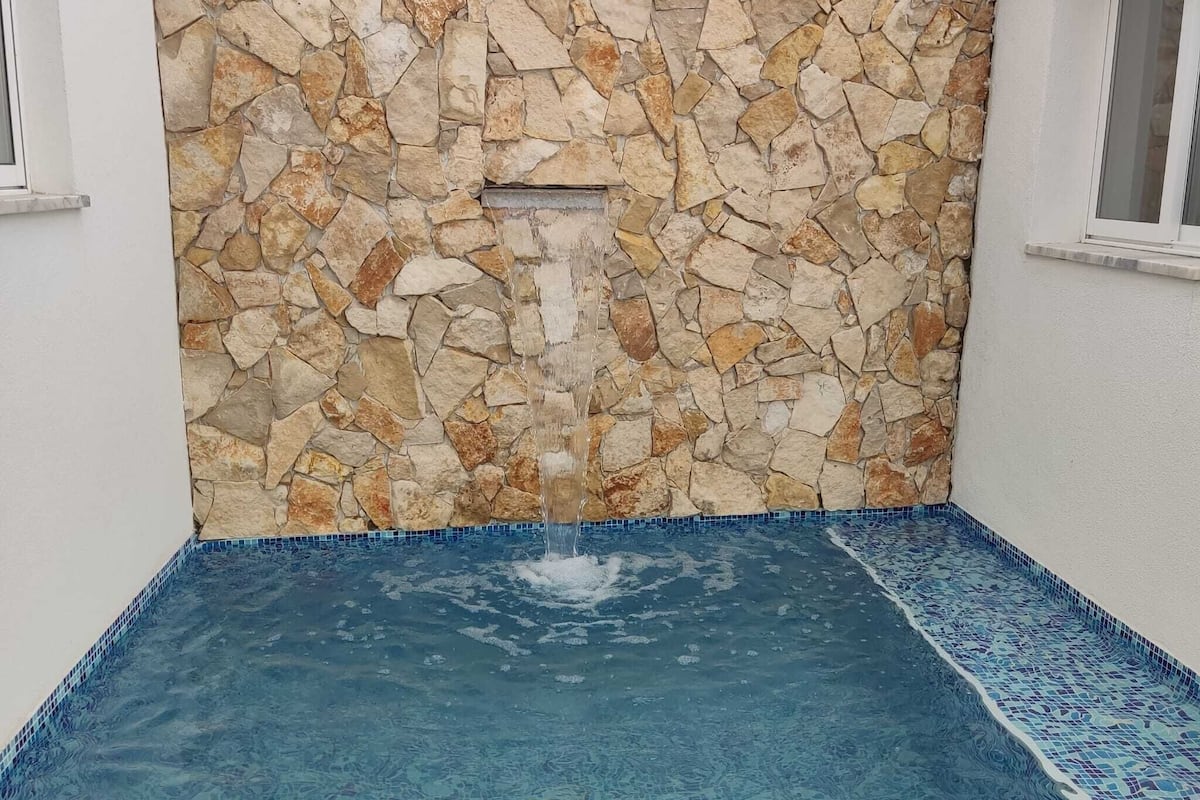 Un mur de pierre agrémenté d’un élément décoratif aquatique dans un espace piscine.