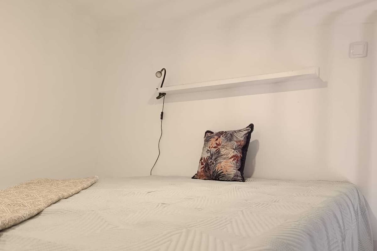 Une chambre à coucher comprenant un lit, un oreiller, une étagère fixée au mur et une prise de courant.