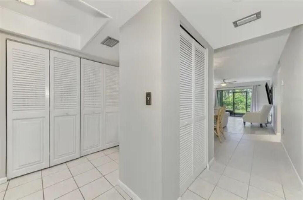 A hallway with white tiled floors, a white door with a handle, and a white wall.