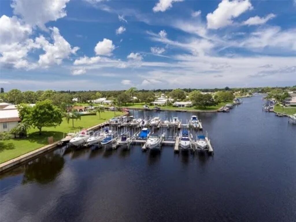 En småbåtshamn med båtar förtöjda längs en kanal, omgiven av grönska och byggnader.