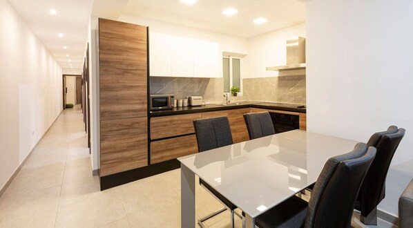 A modern kitchen with a dining area, featuring a large table and chairs, a microwave, and a stove. - Spacious 3BR designer home just off the promenade (San Pawl il-Baħar)