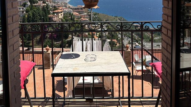 Un balcon avec une table et des chaises, donnant sur une ville côtière et la mer.