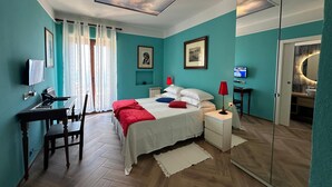 Une chambre à coucher comprenant un lit, des tables de chevet, un bureau, une chaise, un téléviseur et un miroir dans la salle de bain.