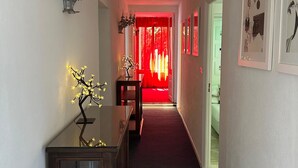 Un couloir avec une moquette sombre, un meuble en bois surmont é d’une vitre, et un rideau rouge au fond.