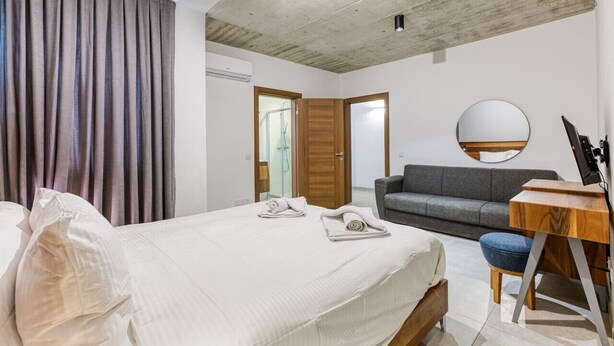 A bedroom with a bed, a gray sofa, a wooden desk, and a mirror on the wall.