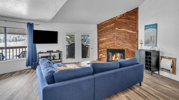 A modern living room with a blue sofa, a fireplace, a TV, and a wooden accent wall.