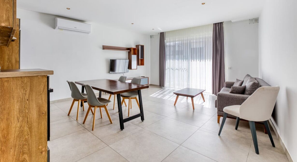 Una sala de estar moderna con comedor, un sofá y un televisor montado en la pared.