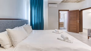 Et hotelværelse med en stor seng, en grå sengegavl, et blåt gardin og en trædør.