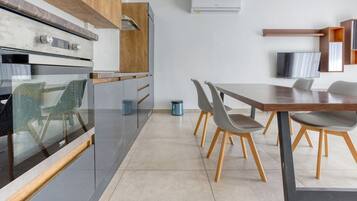A modern kitchen with a built-in oven, a dining area with a wooden table and chairs, and a TV mounted on the wall.
