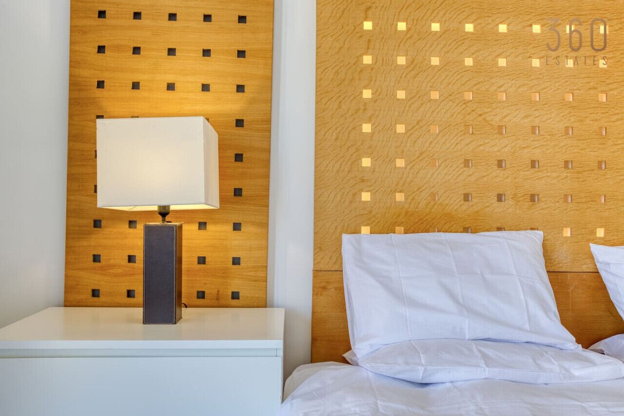 Una habitación de hotel con cabecera de madera, una mesita de noche con lámpara y una cama con ropa blanca de cama.